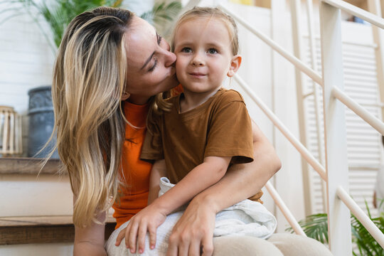 Blond mother kissing cute boy on stairs of house