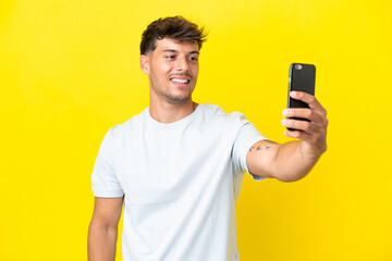 Young caucasian handsome man isolated on yellow background making a selfie with mobile phone