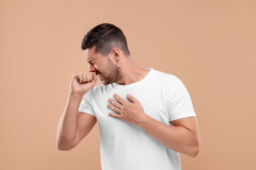 Allergy symptom. Man sneezing on light brown background