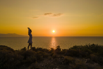 Fototapeta premium Woman in dress stand on seacoast during sunset at seascape. concept of healthy lifestyle and love of life