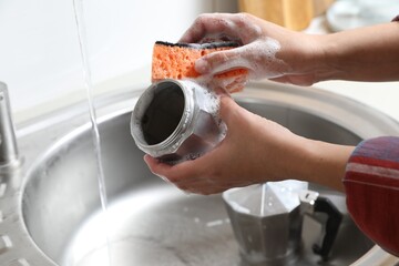 Woman washing moka pot (coffee maker) above sink in kitchen, closeup
