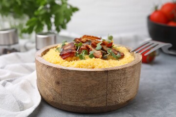 Cooked cornmeal with bacon and microgreens in bowl on light grey table, closeup