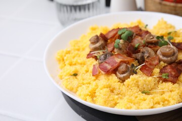 Tasty cornmeal with bacon, mushrooms and microgreens in bowl on white table, closeup. Space for text