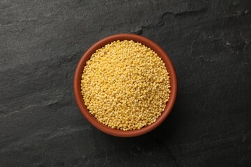 Millet groats in bowl on black table, top view