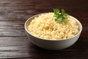 Delicious bulgur with parsley in bowl on wooden table, closeup. Space for text