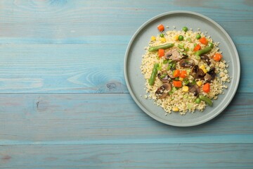 Delicious bulgur with vegetables and mushrooms on light blue wooden table, top view. Space for text