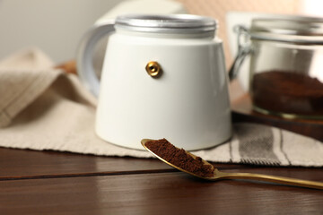 Moka pot and spoon with ground coffee on wooden table, closeup