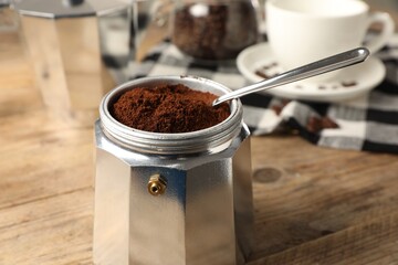 Moka pot and spoon with ground coffee on wooden table, closeup