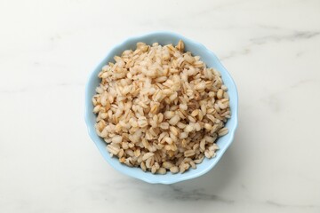 Delicious pearl barley in bowl on white marble table, top view