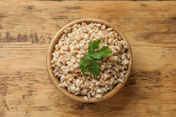 Delicious pearl barley with parsley in bowl on wooden table, top view