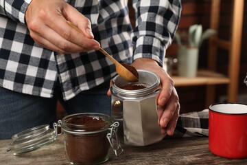 Fototapeta na wymiar Man putting ground coffee into moka pot at table in kitchen, closeup