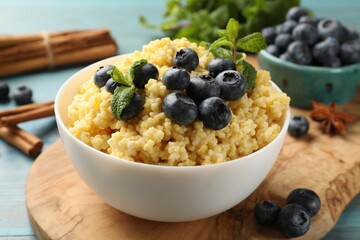 Tasty millet porridge with blueberries and mint in bowl on light blue wooden table, closeup