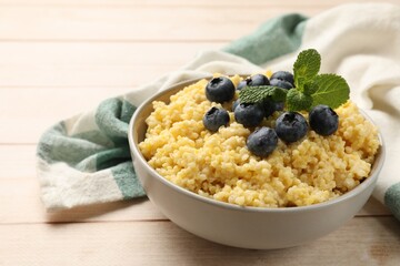 Tasty millet porridge with blueberries and mint in bowl on light wooden table, closeup. Space for text