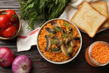Delicious red lentils with mushrooms and dill in bowl served on wooden table, flat lay