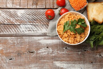 Delicious red lentils with parsley, tomatoes and bread on wooden table, flat lay. Space for text