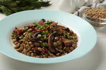 Delicious lentils with mushrooms, bacon and green onion on white table, closeup
