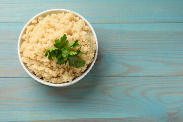 Tasty quinoa porridge with parsley in bowl on light blue wooden table, top view. Space for text