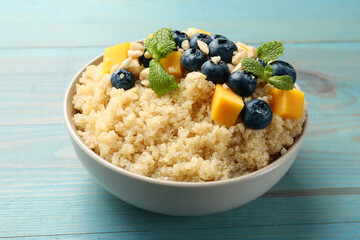 Tasty quinoa porridge with blueberries, pumpkin and mint in bowl on light blue wooden table, closeup
