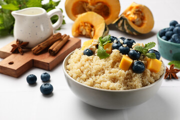 Tasty quinoa porridge with blueberries, pumpkin and mint in bowl on white table