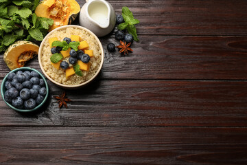 Flat lay composition with bowl of tasty quinoa porridge, pumpkin and blueberries on wooden table. Space for text