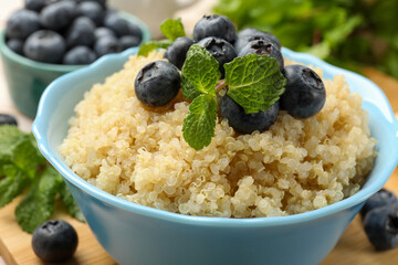 Tasty quinoa porridge with blueberries and mint in bowl on table, closeup