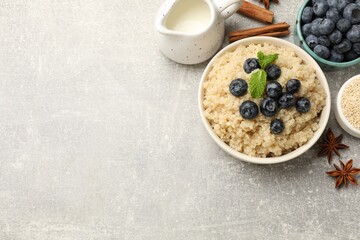 Flat lay composition with bowl of tasty quinoa porridge and blueberries on light grey table. Space for text