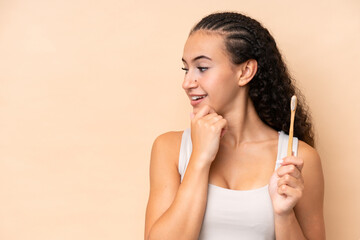 Young woman brushing teeth isolated on beige background thinking an idea and looking side