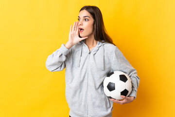 Young football player woman isolated on yellow background shouting with mouth wide open to the side