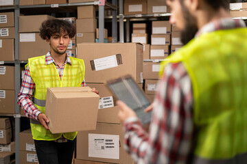 Warehouse workers preparing a shipment in a large storehouse. Two warehouse workers using a digital...