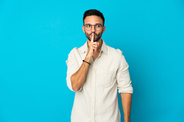 Young caucasian man isolated on blue background showing a sign of silence gesture putting finger in mouth