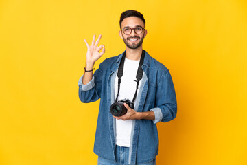 Young photographer girl isolated on yellow background showing ok sign with fingers