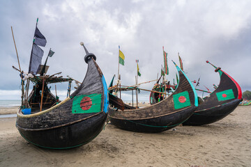 View of three traditional wooden fishing boats known as moon boats resting on beach near Cox's Bazar, Bangladesh under cloudy sky