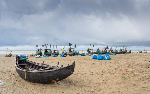 Moody landscape view of traditional wooden fishing boats known as moon boats on beach under cloudy sky, Cox's Bazar, Bangladesh