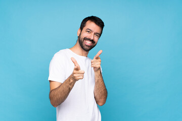 Young man with beard  over isolated blue background pointing to the front and smiling