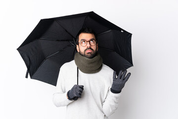 Caucasian handsome man with beard holding an umbrella over isolated white wall frustrated by a bad situation