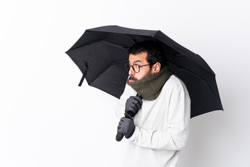 Caucasian handsome man with beard holding an umbrella over isolated white wall