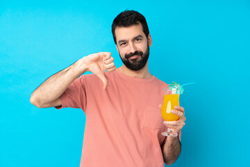 Young man over holding a cocktail over isolated blue background showing thumb down