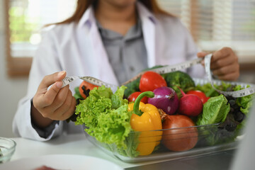 Nutritionist holding plate full of fresh vegetables and measuring tape. Weight loss and healthy eating concept.