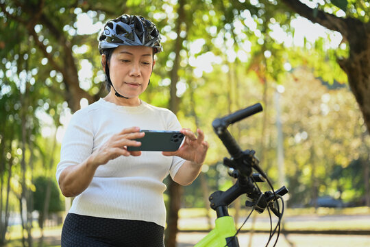 Image of active senior woman using mobile phone resting after morning cycling outdoors.