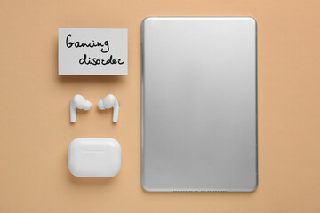 Card with phrase Gaming Disorder, earphones and tablet on beige background, flat lay. Addictive...