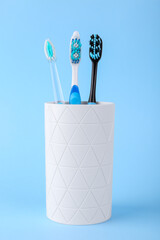 Different toothbrushes in holder on light blue background