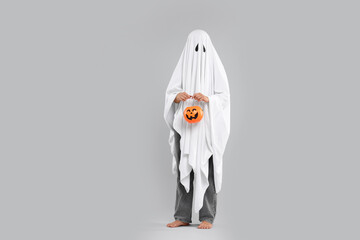 Woman in white ghost costume holding pumpkin bucket on light grey background. Halloween celebration