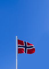 Vertical photo of a bright fluttering Norwegian flag on a flagpole against a clear blue sky