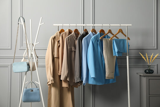 Rack with different stylish women`s clothes and bags near grey wall