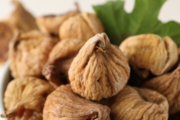 Tasty dried figs and green leaf in bowl, closeup