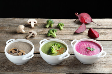 Different tasty cream soups in bowls and ingredients on old wooden table