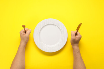 Man with fork, knife and empty plate at yellow table, top view