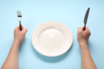 Man with cutlery and empty plate at light blue table, closeup