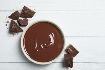 Tasty milk chocolate paste in bowl and pieces on white wooden table, flat lay. Space for text