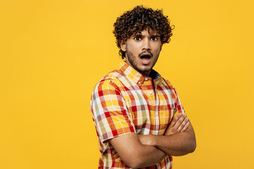 Side view young sad frowning shocked mad Indian man he wearing shirt casual clothes hold hands crossed folded look camera isolated on plain yellow color background studio portrait. Lifestyle concept.